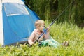 Cute small boy sits near a tent with a fishing rod in his hands. Royalty Free Stock Photo