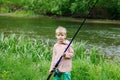 Cute small boy stand near a river with a fishing rod in his hands. Royalty Free Stock Photo