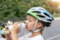 Cute small caucasian girl kid in safety sport helmet drinking fresh water from bottle after exercise bike, scooter or Royalty Free Stock Photo