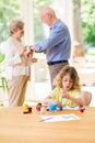 Cute child sitting at the table and painting a picture for grandpa and grandma standing behind him