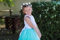 Cute small girl dressed in blue and white dress with a wreath of artificial flowers on her head, child in a festive dress on a nat