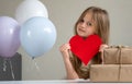 Cute small girl holding big red heart near air balloons and gifts. Valentines Day, love, mothers fathers Day, romantic