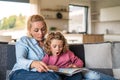 A cute small girl with mother on sofa indoors at home, reading book. Royalty Free Stock Photo
