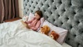 A cute small happy girl enjoying lying in a huge bed covered with blanket smiling and reading her book aloud Royalty Free Stock Photo