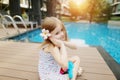 Cute small human girl kid sitting close to swimming pool wearing flower on sunny day Royalty Free Stock Photo