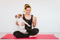 Cute small jack russell dog doing yoga on a mat at home with her owner. Young woman listening to music on yellow mobile phone and Royalty Free Stock Photo