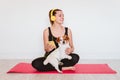 Cute small jack russell dog doing yoga on a mat at home with her owner. Young woman listening to music on yellow mobile phone and Royalty Free Stock Photo