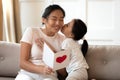 Cute small vietnamese baby girl kissing smiling mommy, congratulating indoors.