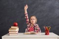 Cute smart girl raised hand while sitting at table