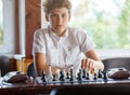 Cute, smart, 11 years old boy in white shirt sits in the classroom and plays chess on the chessboard. Training, lesson, hobby