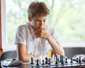 Cute, smart, 11 years old boy in white shirt sits in the classroom and plays chess on the chessboard. Training, lesson, hobby Royalty Free Stock Photo