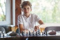 Cute, smart, 11 years old boy in white shirt sits in the classroom and plays chess on the chessboard. Training, lesson, hobby Royalty Free Stock Photo