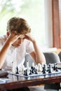 Cute, smart, 11 years old boy in white shirt sits in the classroom and plays chess on the chessboard. Training, lesson, hobby Royalty Free Stock Photo