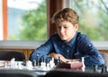 Cute, smart, 11 years old boy in white shirt sits in the classroom and plays chess on the chessboard. Training, lesson, hobby