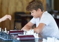 Cute, smart, 11 years old boy in white shirt sits in the classroom and plays chess on the chessboard. Training, lesson, hobby Royalty Free Stock Photo