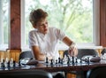 Cute, smart, young boy in white shirt plays chess on the chessboard in the classroom. Education, hobby, training Royalty Free Stock Photo