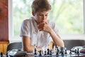 Cute, smart, young boy in white shirt plays chess on the chessboard in the classroom. Education, hobby, training