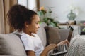 Cute smiling Afro-American little girl using laptop and smiling while sitting on sofa. Royalty Free Stock Photo