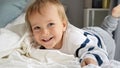 Cute smiling baby boy with blond hair and blue eyes lying in bed and smiling in camera Royalty Free Stock Photo