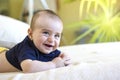 Cute Smiling baby boy with blue T-shirt in white sunny bedroom with green plant. Royalty Free Stock Photo