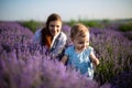 Cute smiling baby girl with blonde curly hair wearing a blue dress walking on a lavender field. Mother and baby daughter having fu Royalty Free Stock Photo