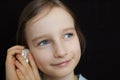 Cute smiling blonde girl holding seashell next to her ear and listening to the ocean on black background in studio Royalty Free Stock Photo