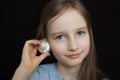 Cute smiling blonde girl holding seashell next to her ear and listening to the ocean on black background in studio Royalty Free Stock Photo