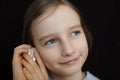 Cute smiling blonde girl holding seashell next to her ear and listening to the ocean on black background in studio Royalty Free Stock Photo