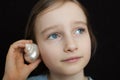 Cute smiling blonde girl holding seashell next to her ear and listening to the ocean on black background in studio Royalty Free Stock Photo