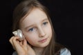 Cute smiling blonde girl holding seashell next to her ear and listening to the ocean on black background in studio Royalty Free Stock Photo