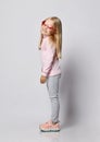 Side view portrait of blonde kid girl in stylish smoked heart-shaped sunglasses, turtleneck shirt sweater and pants Royalty Free Stock Photo