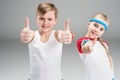 Cute smiling boy and girl in sportswear showing thumbs up on grey Royalty Free Stock Photo
