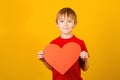 Cute smiling boy holding red paper heart. Child giving valentines heart. Love mood