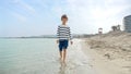 Cute smiling boy in sweater splashing sea water as he walks on sandy beach. Holiday, vacation, weekend at nature Royalty Free Stock Photo