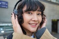 Cute smiling brunette girl, listens music in headphones and looking happy at camera, stands on street, commutes, waits Royalty Free Stock Photo