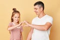 Cute smiling brwon haired little girl standing with her father and making heart shape with hands together expressing love family
