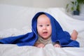 Cute smiling caucasian infant baby looking at camera in blue towel after bathing in the bath on white bed.Copyspace. Royalty Free Stock Photo