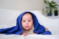Cute smiling caucasian infant baby looking at camera in blue towel after bathing in the bath on white bed.Copyspace. Royalty Free Stock Photo