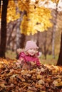 Cute smiling child girl having fun on the autumn walk and sitting in leaves Royalty Free Stock Photo