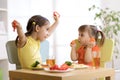 Cute smiling child and toddler girls playing and eating spaghetti with vegetables for healthy lunch sitting in a white sunny kitch Royalty Free Stock Photo