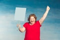 Cute smiling chubby red-haired woman screaming fervently, waving his hand in the second holds a protest poster on a blue