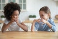 Cute smiling diverse little girls drinking fresh water in kitchen