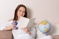 Cute smiling girl with a blue Cup and the diary, sitting on the couch in the room and reads. Royalty Free Stock Photo