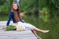 Cute smiling girl with a bouquet of daisies on the pier barefoot dreaming.