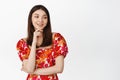 Cute smiling girl looking pleased aside, gazing at logo or brand name, wearing red floral dress against white background Royalty Free Stock Photo