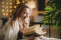 Cute smiling girl reading a book while sitting on her bed at home in the evening Royalty Free Stock Photo