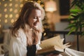 Cute smiling girl reading a book while sitting on her bed at home in the evening Royalty Free Stock Photo