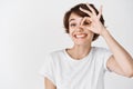 Cute smiling girl showing okay sign on eye and looking happy, praising perfect product, standing in t-shirt against