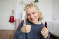 Cute smiling girl shows lipstick and thumbs up hand sign, recommending beauty product, records content for social media Royalty Free Stock Photo