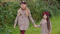 Cute smiling girls in berets holding hands and walking in garden